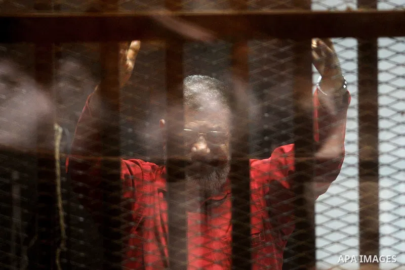 Egypt's ousted Islamist president Mohamed Morsi, wearing a red uniform, gestures from behind the bars during his trial at the police academy in Cairo on April 23, 2016. An Egyptian court postponed its verdict and sentenc...