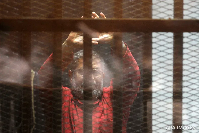 Egypt's ousted Islamist president Mohamed Morsi, wearing a red uniform, gestures from behind the bars during his trial at the police academy in Cairo on April 23, 2016. An Egyptian court postponed its verdict and sentenc...