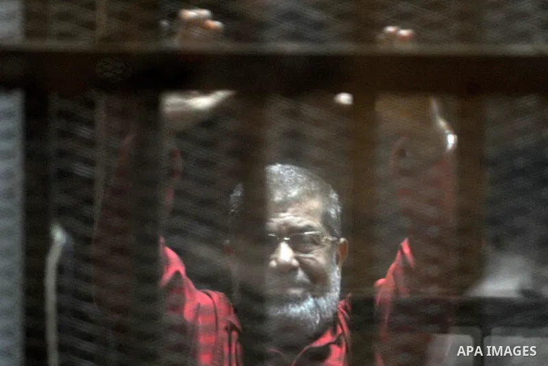 Egypt's ousted Islamist president Mohamed Morsi, wearing a red uniform, gestures from behind the bars during his trial at the police academy in Cairo on April 23, 2016. An Egyptian court postponed its verdict and sentenc...