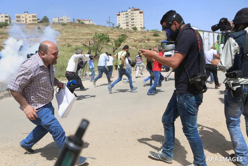 Palestinian journalists run for cover from a tear gas canister fired by Israeli troops during a protest calling for the release of Palestinian journalist Omar Nazal, who is held by Israel, near Israel's Ofer Prison near...
