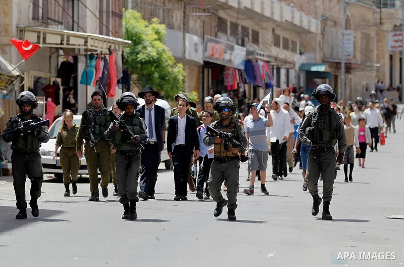 Israeli troops stand guard as Israeli settlers have a tour during the Jewish holiday of Passover in the West Bank city of Hebron, on April 26, 2016. Photo by Wisam Hashlamoun