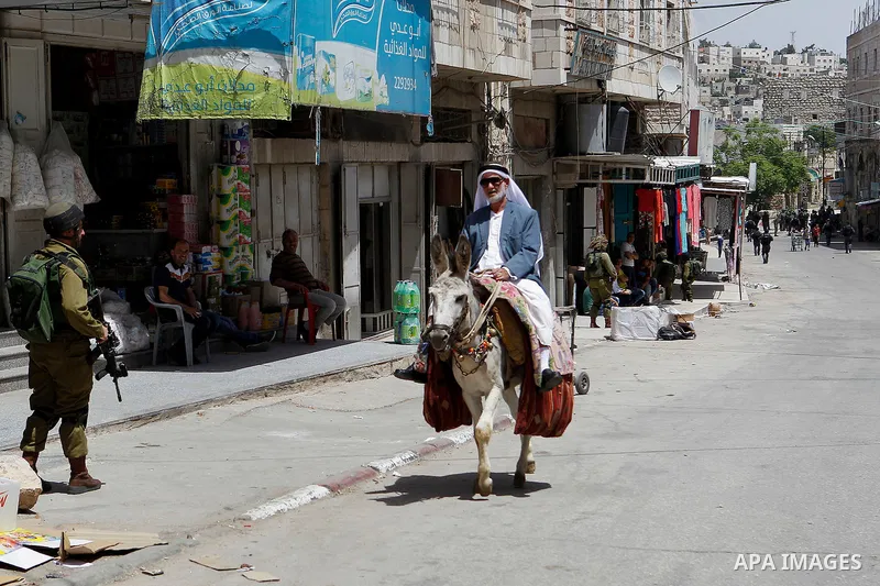 A Palestinian man rides a donkey as Israeli settlers have a tour during the Jewish holiday of Passover in the West Bank city of Hebron, on April 26, 2016. Photo by Wisam Hashlamoun
