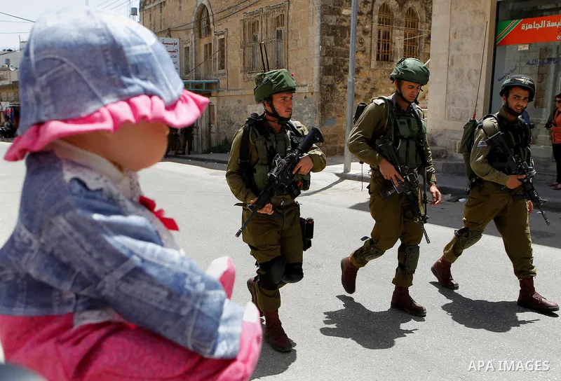 Israeli troops stand guard as Israeli settlers have a tour during the Jewish holiday of Passover in the West Bank city of Hebron, on April 26, 2016. Photo by Wisam Hashlamoun