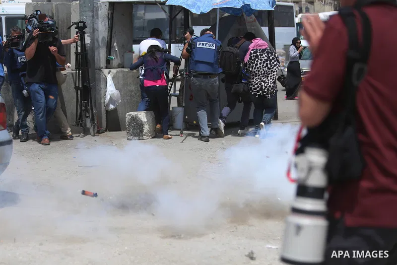Palestinian journalists run for cover from a tear gas canister fired by Israeli security forces at the Qalandia checkpoint, between Jerusalem and Ramallah in the Israeli occupied West Bank, after two Palestinians were sh...
