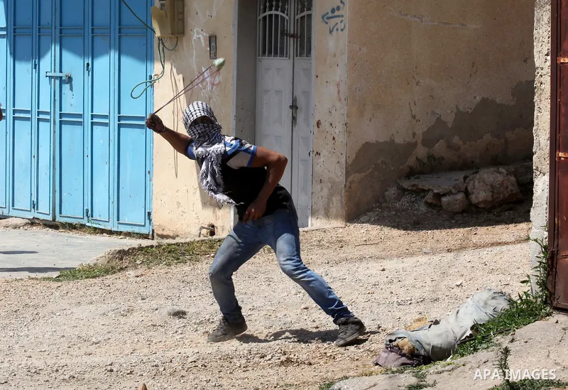 A Palestinian protester uses a slingshot to hurl stones towards Israeli security forces during clashes following a demonstration against the expropriation of Palestinian land by Israel on April 29, 2016 in the village of...
