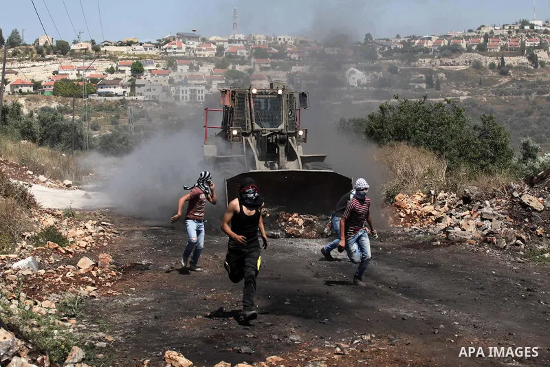 Palestinian protesters run away from a digger operated by Israeli security forces during clashes following a demonstration against the expropriation of Palestinian land by Israel on April 29, 2016 in the village of Kfar...