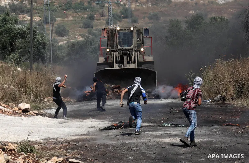 Palestinian protesters hurl stones towards a digger operated by Israeli security forces during clashes following a demonstration against the expropriation of Palestinian land by Israel on April 29, 2016 in the village of...