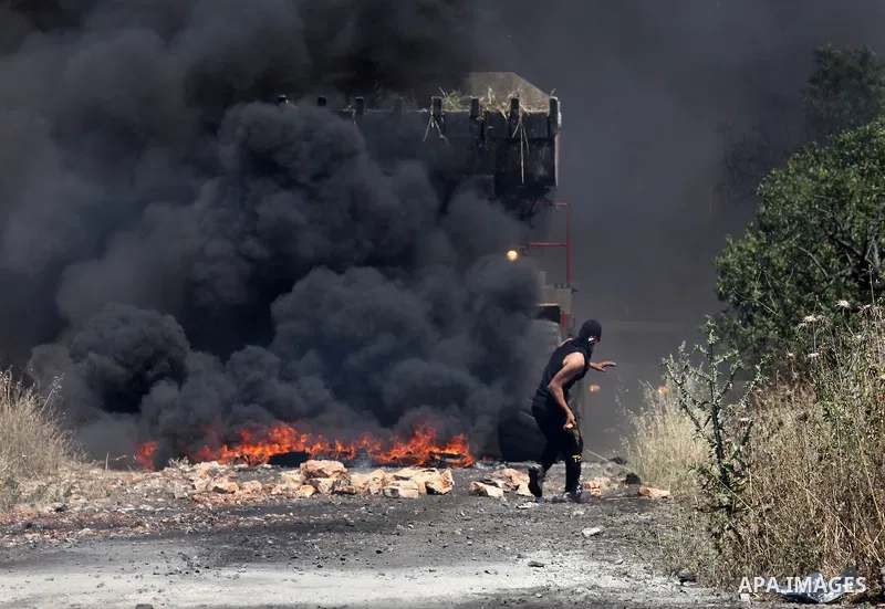 A Palestinian protester hurls stones towards a digger operated by Israeli security forces during clashes following a demonstration against the expropriation of Palestinian land by Israel on April 29, 2016 in the village...
