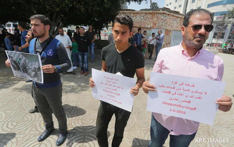 Syrians who live in the Gaza Strip after fleeing their war-hit country hold placards during a rally against Syrian government shelling on the northern city of Aleppo, on May 1, 2016, in Gaza City. Photo by Mohammed Asad