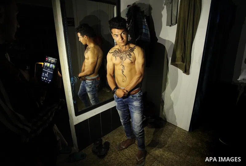 A bodybuilder reacts after his body was painted with Arabic letters by Palestinian artist Bilal Khaled at a gym in Khan Younis in the southern Gaza strip, on May 3, 2016. Photo by Ashraf Amra