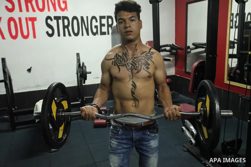 A bodybuilder reacts after his body was painted with Arabic letters by Palestinian artist Bilal Khaled at a gym in Khan Younis in the southern Gaza strip, on May 3, 2016. Photo by Ashraf Amra