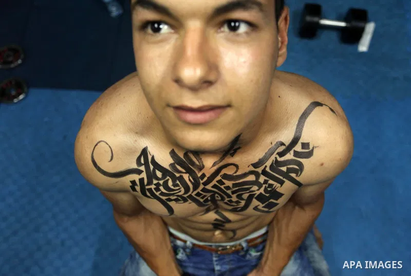 A bodybuilder reacts after his body was painted with Arabic letters by Palestinian artist Bilal Khaled at a gym in Khan Younis in the southern Gaza strip, on May 3, 2016. Photo by Ashraf Amra
