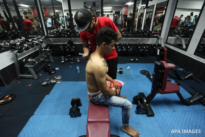 A Palestinian artist Bilal Khalid paints Arabic letters on a bodybuilder body at a gym in Khan Younis in the southern Gaza strip, on May 3, 2016. Photo by Ashraf Amra