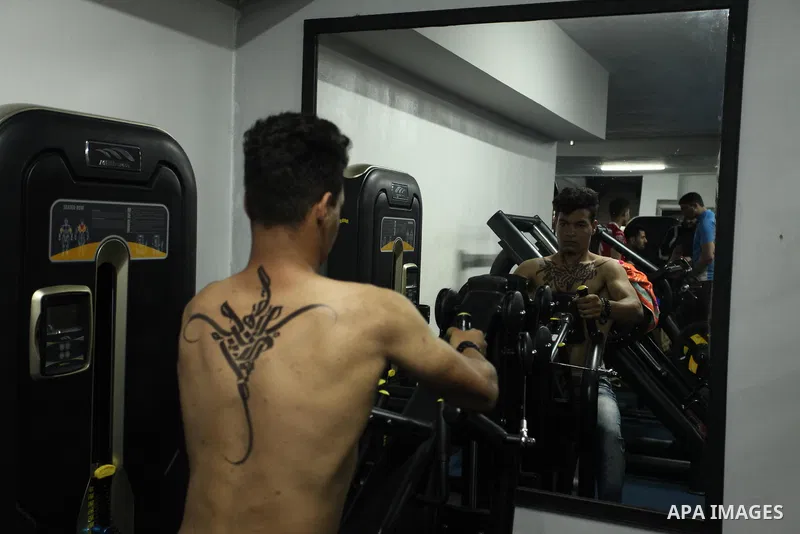 A bodybuilder reacts after his body was painted with Arabic letters by Palestinian artist Bilal Khaled at a gym in Khan Younis in the southern Gaza strip, on May 3, 2016. Photo by Ashraf Amra