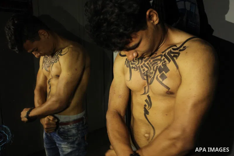 A bodybuilder reacts after his body was painted with Arabic letters by Palestinian artist Bilal Khaled at a gym in Khan Younis in the southern Gaza strip, on May 3, 2016. Photo by Ashraf Amra