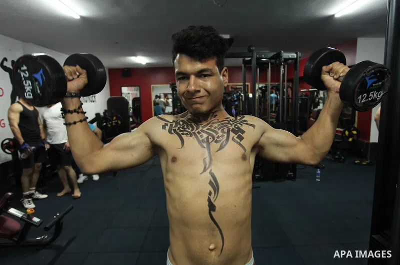 A bodybuilder reacts after his body was painted with Arabic letters by Palestinian artist Bilal Khaled at a gym in Khan Younis in the southern Gaza strip, on May 3, 2016. Photo by Ashraf Amra