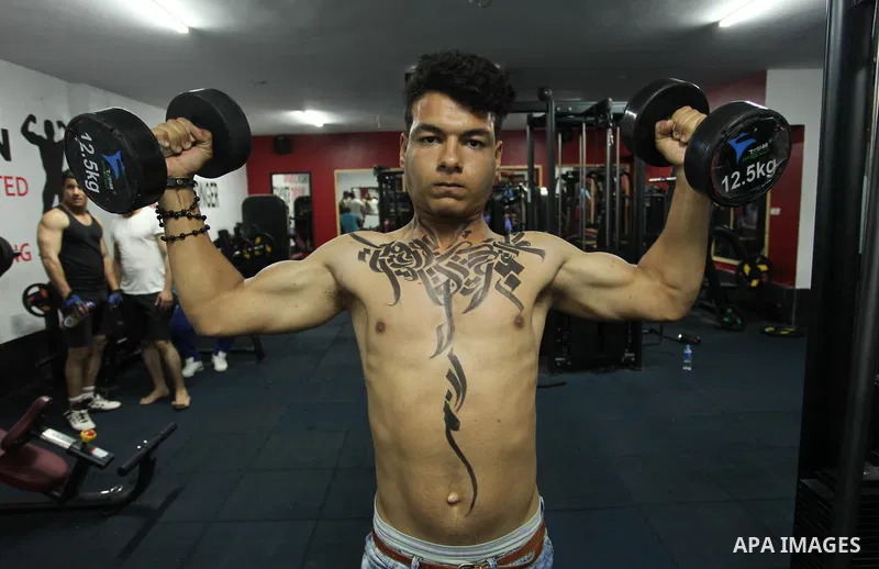 A bodybuilder reacts after his body was painted with Arabic letters by Palestinian artist Bilal Khaled at a gym in Khan Younis in the southern Gaza strip, on May 3, 2016. Photo by Ashraf Amra