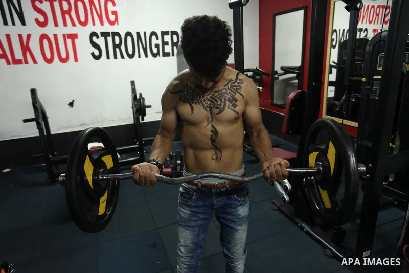 A bodybuilder reacts after his body was painted with Arabic letters by Palestinian artist Bilal Khaled at a gym in Khan Younis in the southern Gaza strip, on May 3, 2016. Photo by Ashraf Amra