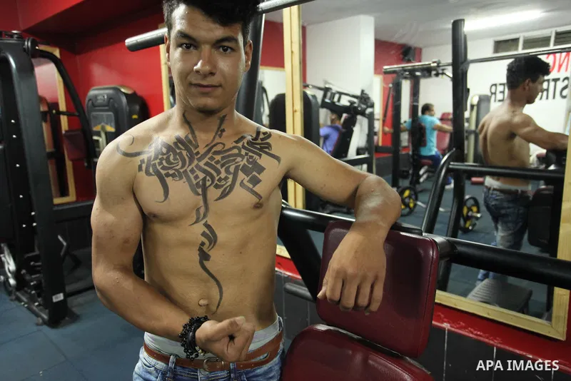 A bodybuilder reacts after his body was painted with Arabic letters by Palestinian artist Bilal Khaled at a gym in Khan Younis in the southern Gaza strip, on May 3, 2016. Photo by Ashraf Amra