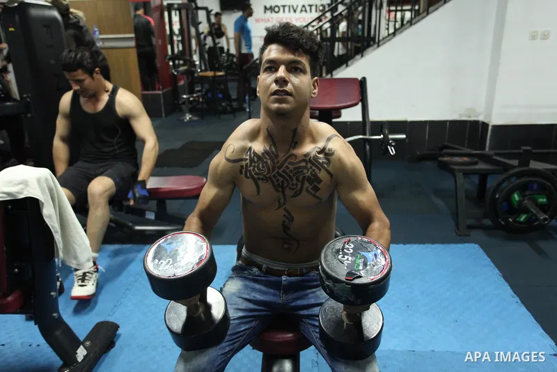 A bodybuilder reacts after his body was painted with Arabic letters by Palestinian artist Bilal Khaled at a gym in Khan Younis in the southern Gaza strip, on May 3, 2016. Photo by Ashraf Amra