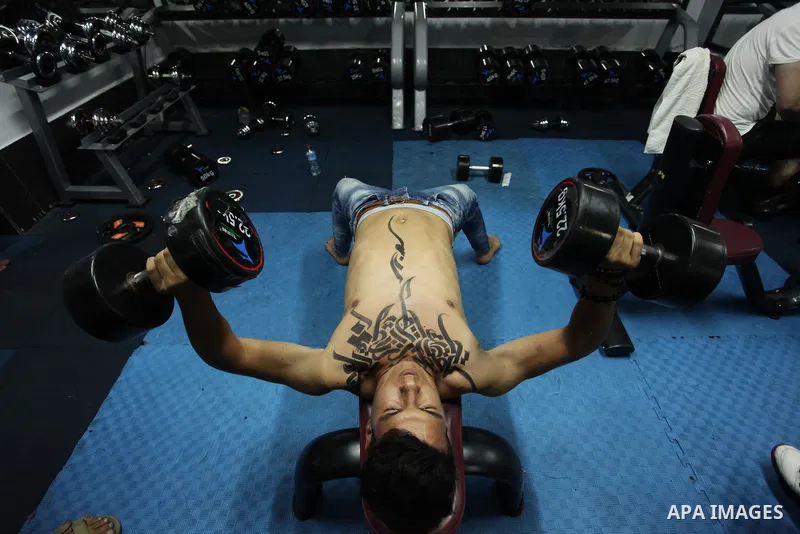 A bodybuilder reacts after his body was painted with Arabic letters by Palestinian artist Bilal Khaled at a gym in Khan Younis in the southern Gaza strip, on May 3, 2016. Photo by Ashraf Amra
