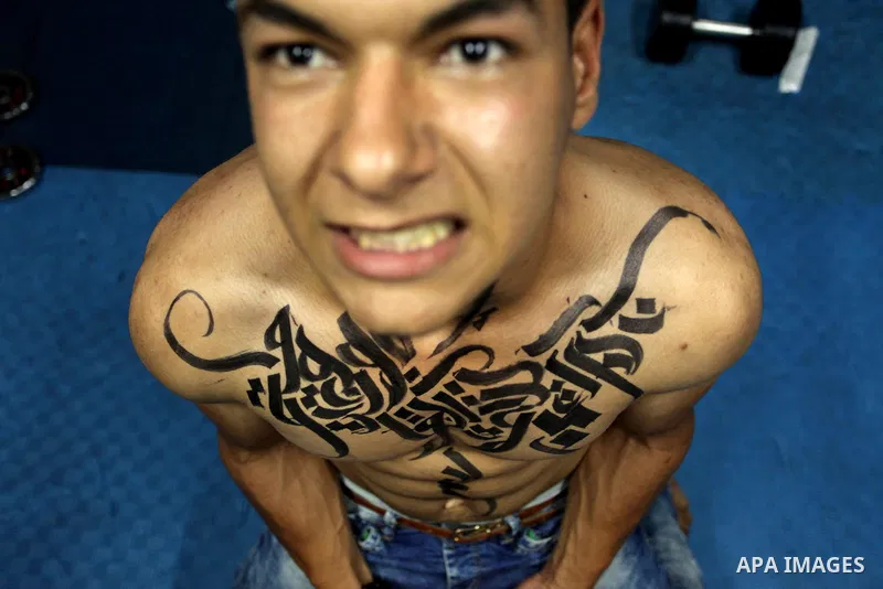 A bodybuilder reacts after his body was painted with Arabic letters by Palestinian artist Bilal Khaled at a gym in Khan Younis in the southern Gaza strip, on May 3, 2016. Photo by Ashraf Amra
