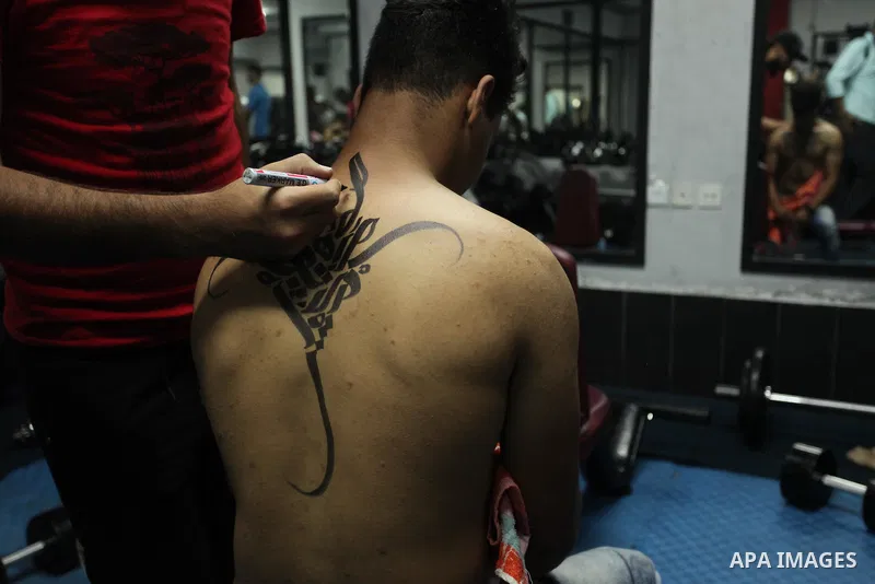 A bodybuilder reacts after his body was painted with Arabic letters by Palestinian artist Bilal Khaled at a gym in Khan Younis in the southern Gaza strip, on May 3, 2016. Photo by Ashraf Amra