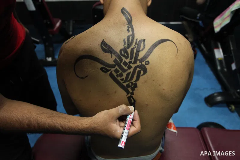 A bodybuilder reacts after his body was painted with Arabic letters by Palestinian artist Bilal Khaled at a gym in Khan Younis in the southern Gaza strip, on May 3, 2016. Photo by Ashraf Amra