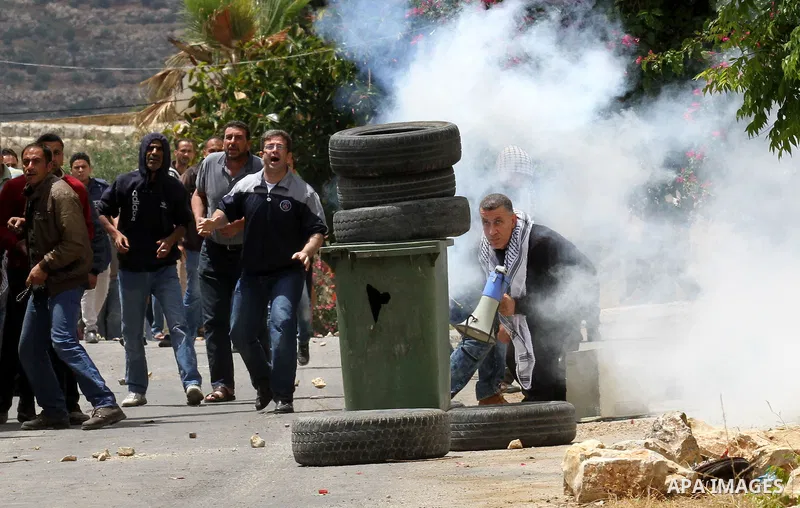 Palestinian protesters take cover from tear gas fired by Israeli security forces during clashes following a demonstration against the expropriation of Palestinian land by Israel on May 06, 2016 in the village of Kfar Qad...