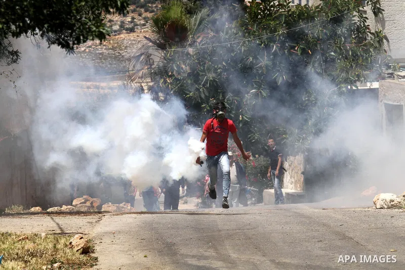 A Palestinian protester throws back a tear gas canister fired by Israeli security forces during clashes following a demonstration against the expropriation of Palestinian land by Israel on May 06, 2016 in the village of...
