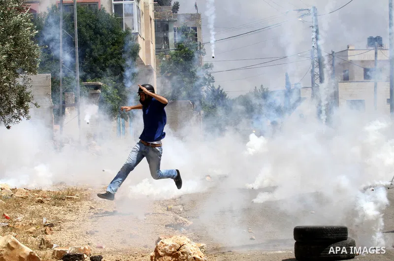 A cameraman takes cover from a tear gas canister fired by Israeli security forces during clashes following a demonstration against the expropriation of Palestinian land by Israel on May 06, 2016 in the village of Kfar Qa...