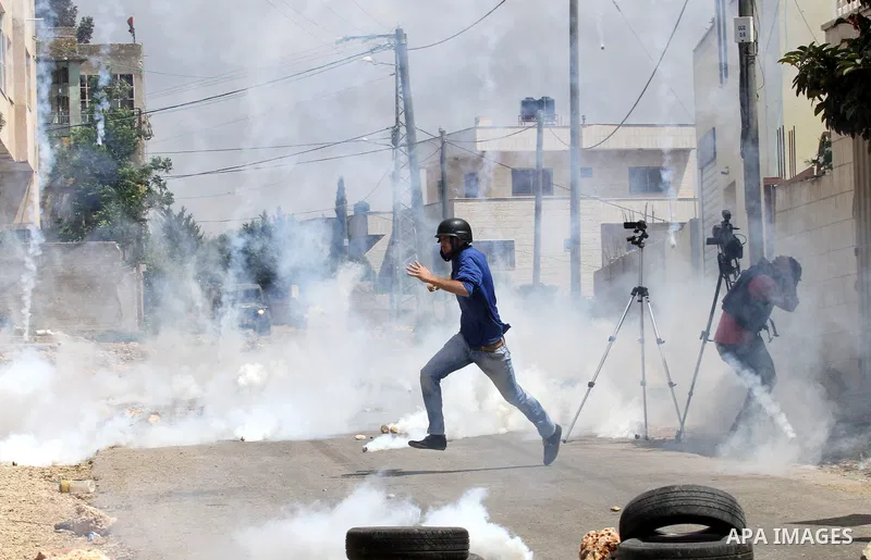 A cameraman takes cover from a tear gas canister fired by Israeli security forces during clashes following a demonstration against the expropriation of Palestinian land by Israel on May 06, 2016 in the village of Kfar Qa...