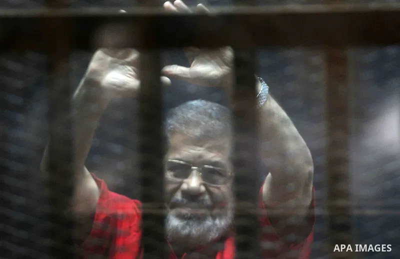 Egypt's ousted Islamist president Mohamed Morsi, wearing a red uniform, gestures from behind the defendant's bars during his trial at the police academy in Cairo on May 7, 2016. An Egyptian court recommended death senten...