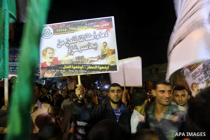 Palestinians hold placards in a protest demanding for end the siege on Gaza and against the killing of three boys from the al-Hindi family, who died in a fire caused by a candle at the family home, in Jabalia in the nort...