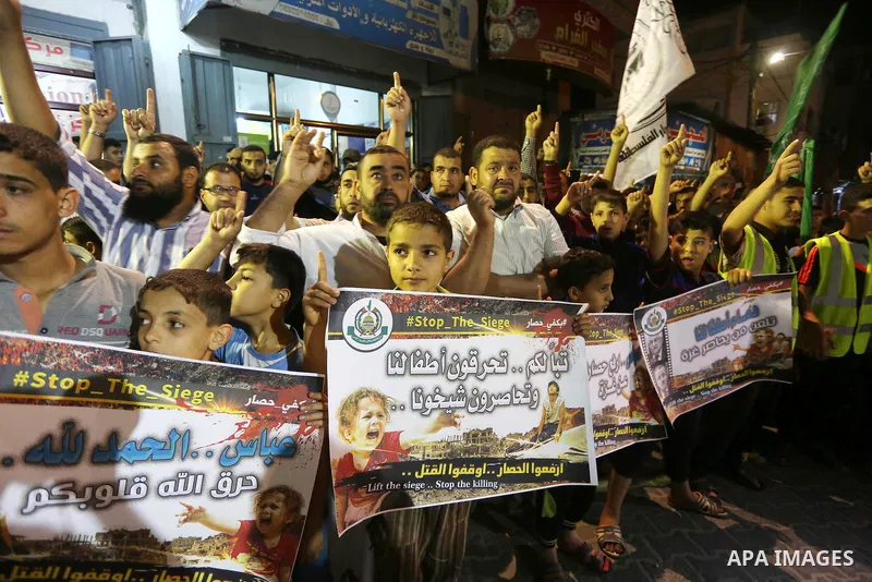 Palestinians hold placards in a protest demanding for end the siege on Gaza and against the killing of three boys from the al-Hindi family, who died in a fire caused by a candle at the family home, in Jabalia in the nort...