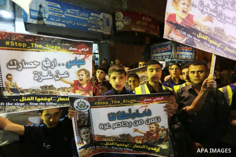 Palestinians hold placards in a protest demanding for end the siege on Gaza and against the killing of three boys from the al-Hindi family, who died in a fire caused by a candle at the family home, in Jabalia in the nort...