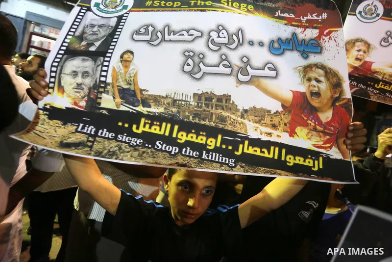 Palestinians hold placards in a protest demanding for end the siege on Gaza and against the killing of three boys from the al-Hindi family, who died in a fire caused by a candle at the family home, in Jabalia in the nort...