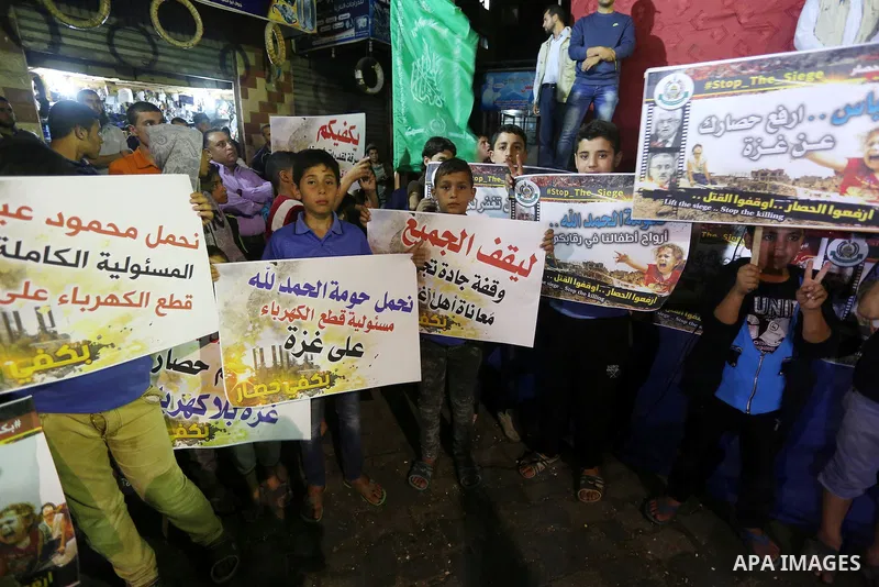 Palestinians hold placards in a protest demanding for end the siege on Gaza and against the killing of three boys from the al-Hindi family, who died in a fire caused by a candle at the family home, in Jabalia in the nort...