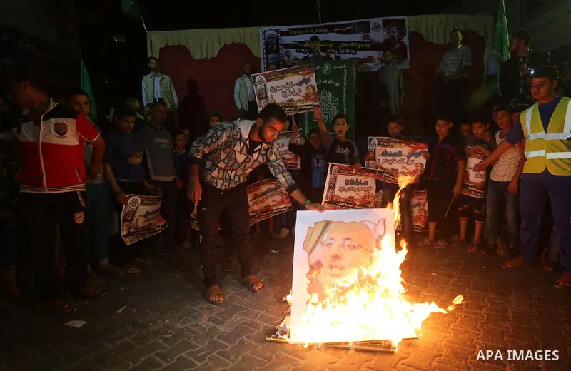 A Palestinian protester burns a poster of Palestinian Prime Minister Rami Hamdallah during a protest demanding for end the siege on Gaza and against the killing of three boys from the al-Hindi family, who died in a fire...
