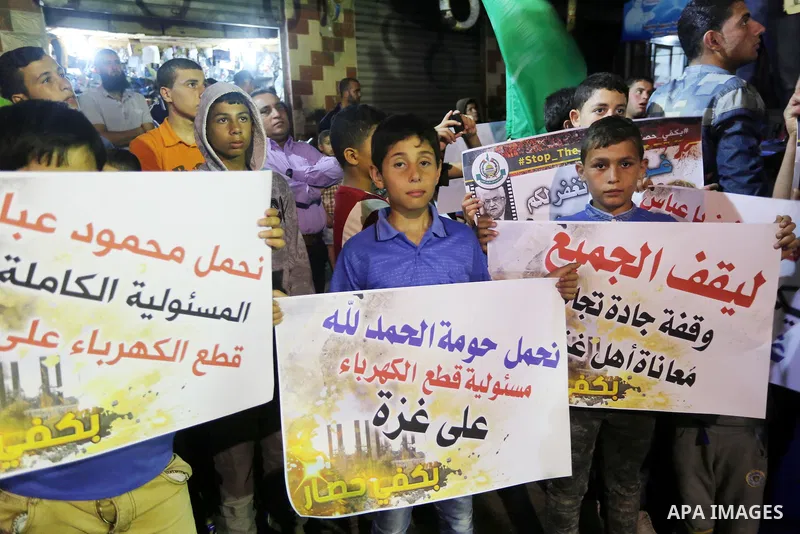 Palestinians hold placards in a protest demanding for end the siege on Gaza and against the killing of three boys from the al-Hindi family, who died in a fire caused by a candle at the family home, in Jabalia in the nort...