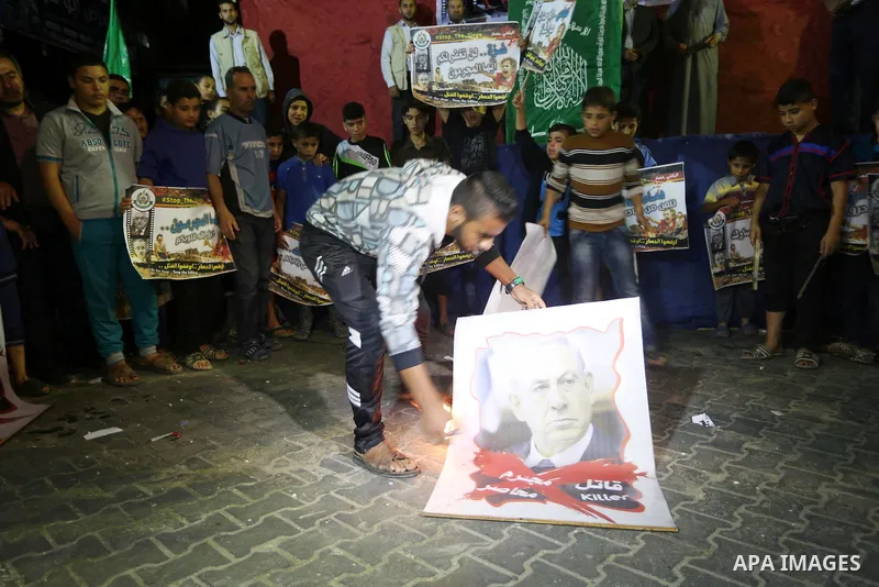 A Palestinian protester burns a poster of Israeli occupation Prime Minister Benjamin Netanyahu during a protest demanding for end the siege on Gaza and against the killing of three boys from the al-Hindi family, who died...