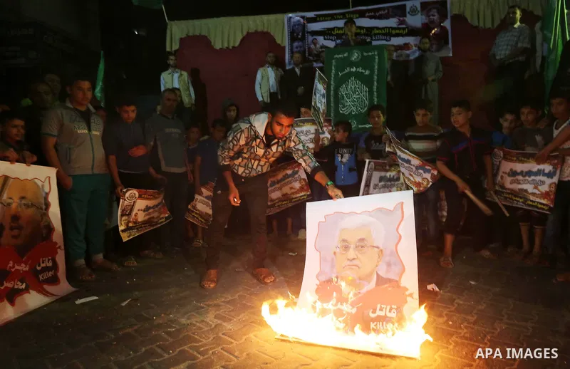 A Palestinian protester burns a poster of Palestinian President Mahmoud Abbas during a protest demanding for end the siege on Gaza and against the killing of three boys from the al-Hindi family, who died in a fire caused...