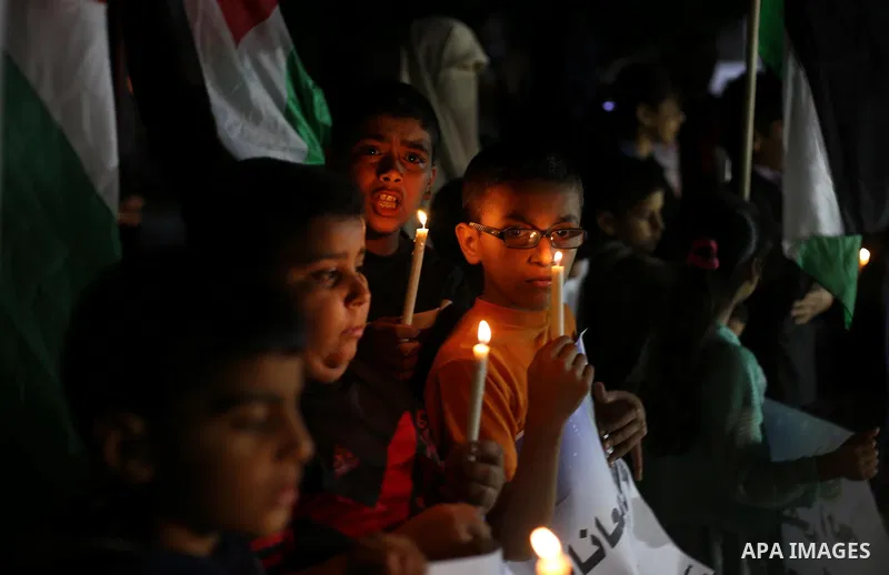 Palestinian children hold placards and light candles during a protest demanding for end the siege on Gaza and against the killing of three boys from the al-Hindi family, who died in a fire caused by a candle at the famil...