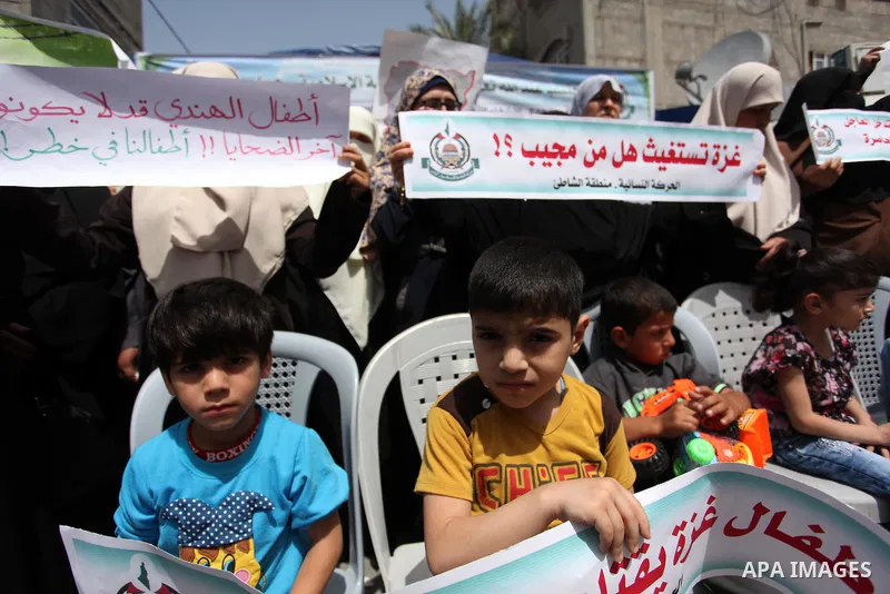 Palestinian children hold placards during a protest against the killing of three boys from the al-Hindi family, who died in a fire caused by a candle at the family home in Gaza city on May 9, 2016. Photo by Ashraf Amra
