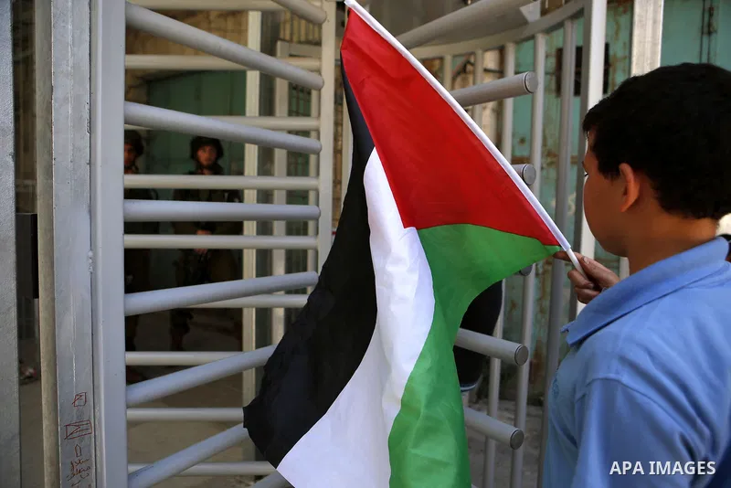 A Palestinian boy holds a national flag during a protest against the closure of Shuhada street to Palestinians in the West Bank city of Hebron on May 12, 2016. Photo by Wisam Hashlamoun