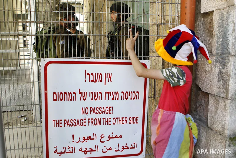 A Palestinian boy dressed as clown flashes victory during a protest against the closure of Shuhada street to Palestinians in the West Bank city of Hebron on May 12, 2016. Photo by Wisam Hashlamoun