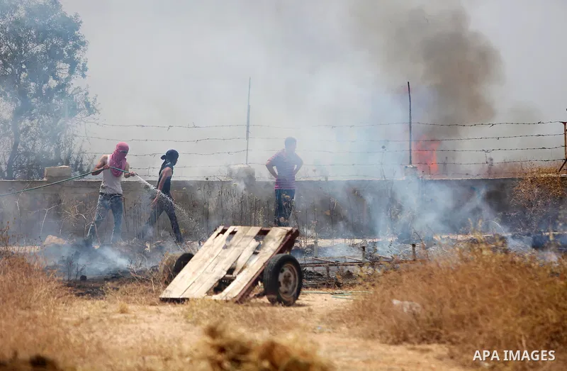 Palestinian protesters use a water hose as he tries to extinguish a fire caused by tear gas fired by Israeli troops during clashes at a protest ahead of Nakba day, in the West Bank village of Bilin near Ramallah May 13,...