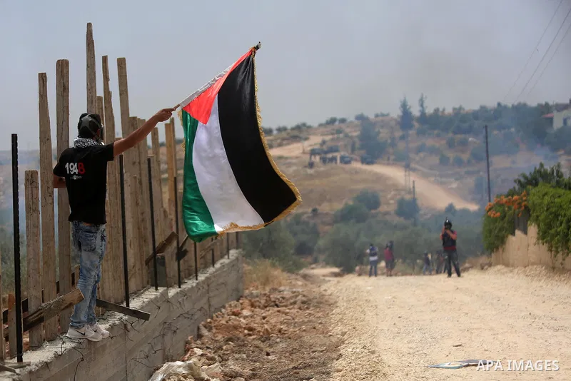 A Palestinian protester holds a Palestinian flag during clashes with Israeli troops at a protest ahead of Nakba day, in the West Bank village of Bilin near Ramallah May 13, 2016. Photo by Shadi Hatem