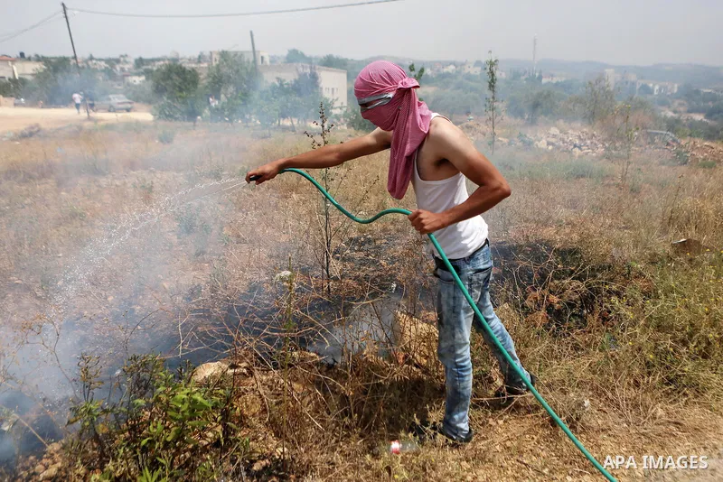 A Palestinian protester uses a water hose as he tries to extinguish a fire caused by tear gas fired by Israeli troops during clashes at a protest ahead of Nakba day, in the West Bank village of Bilin near Ramallah May 13...