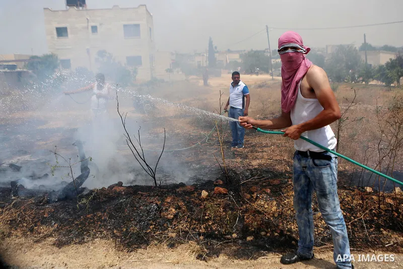 A Palestinian protester uses a water hose as he tries to extinguish a fire caused by tear gas fired by Israeli troops during clashes at a protest ahead of Nakba day, in the West Bank village of Bilin near Ramallah May 13...